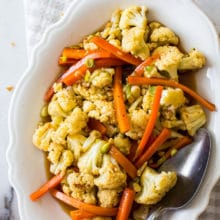 Up close overhead photo of roasted cauliflower and carrots on a white oval dish with a spoon