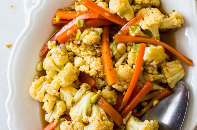 Up close overhead photo of roasted cauliflower and carrots on a white oval dish with a spoon