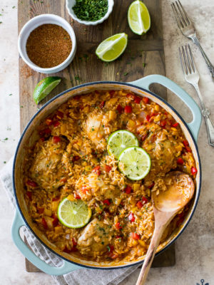 Overhead photo of one pot salsa chicken and rice dinner in a round baking dish surrounded by limes and spices