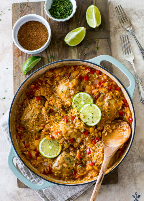 Overhead photo of one pot salsa chicken and rice dinner in a round baking dish surrounded by limes and spices