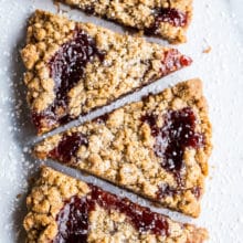 Wedges of jam crumb cookies in a row of six cookies on a light surface