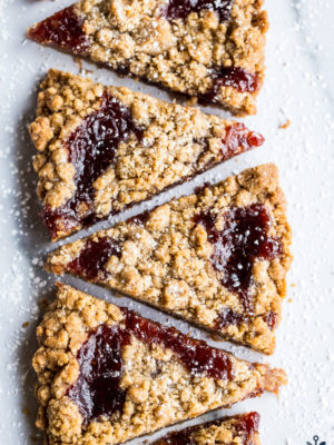 Wedges of jam crumb cookies in a row of six cookies on a light surface