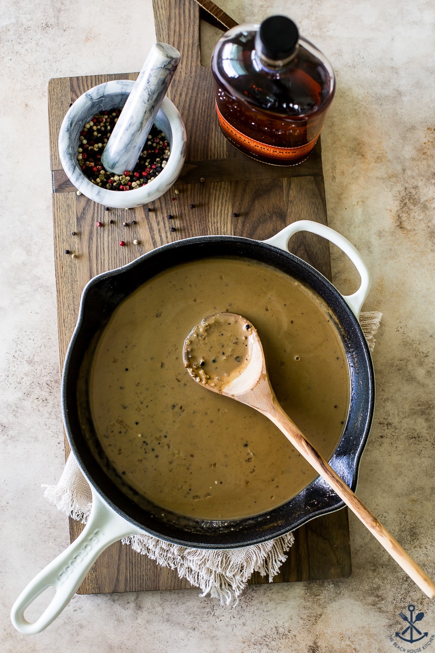 Overhead photo of bourbon peppercorn sauce in a skillet with a wooden spoon inside