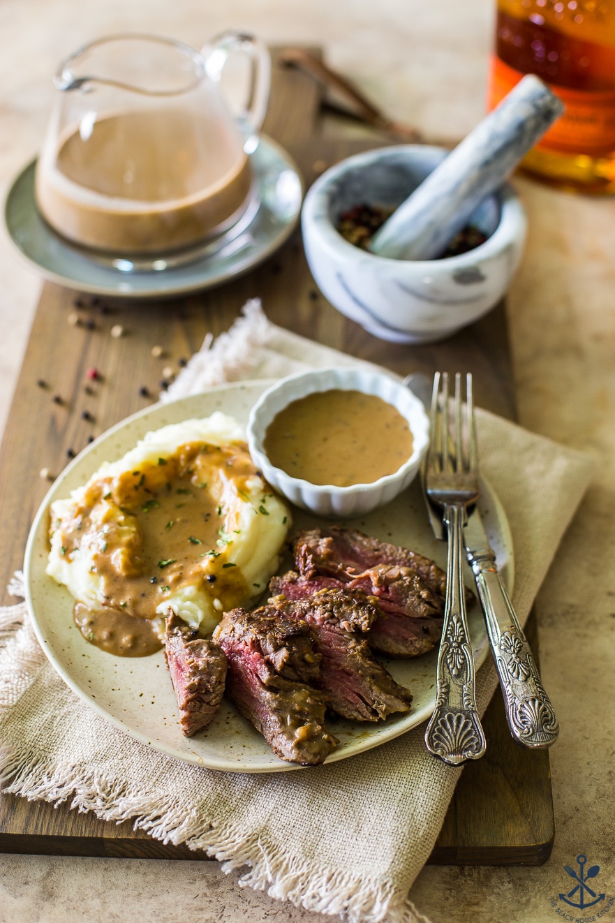 Overehad photo of a plate of steak with mashed potatoes and bourbon peppercorn sauce with a metal fork and a knife on the side
