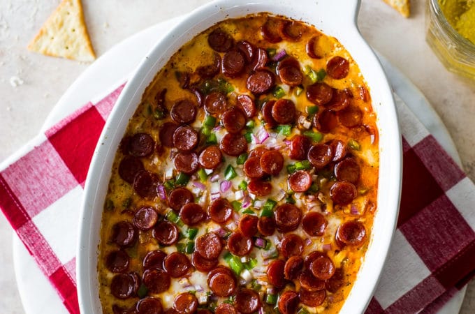Overhead photo of a white oval dish filled with baked pepperoni dip and crackers around