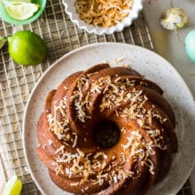 Overhead photo of key lime coconut bundt cake on a gold wire rack with a bowl of toasted coconut