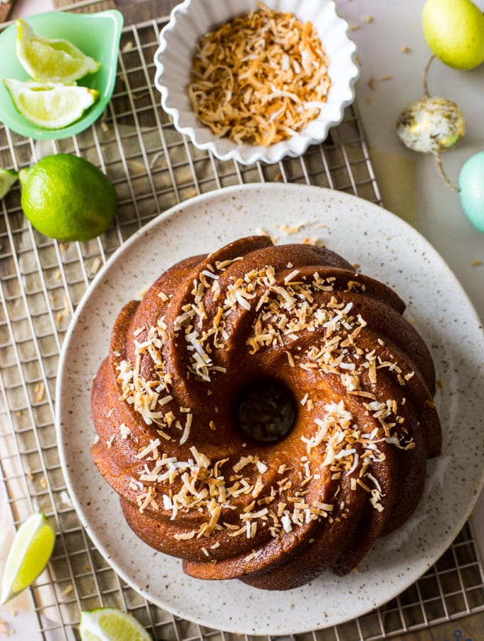 Overhead photo of key lime coconut bundt cake on a gold wire rack with a bowl of toasted coconut