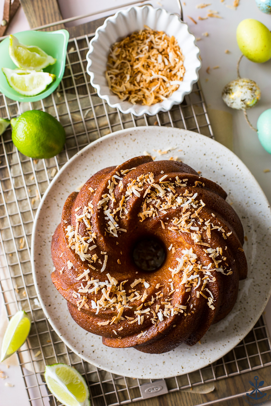 Overhead photo of Key Lime Coconut Bundt Cake on a plate on a wire rack with a bowl of toasted coconut
