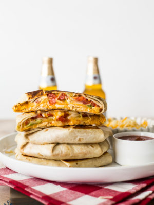 A stack of buffalo chicken crunchwrap supremes with beers in the background