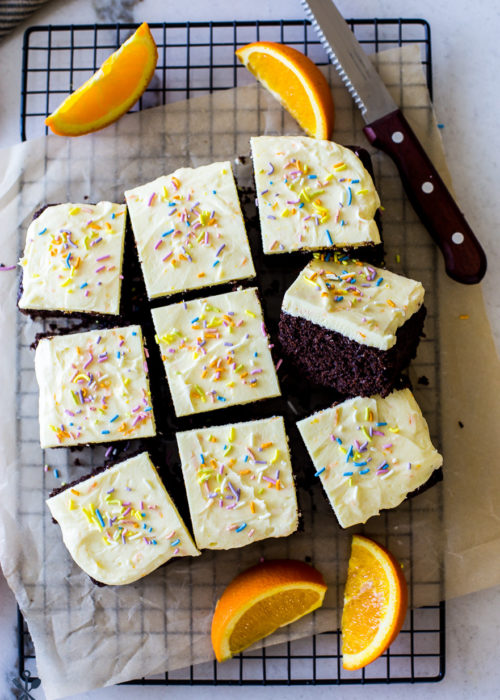 Overhead of the photo of iced chocolate cake surrounded by orange slices and a sharp knife