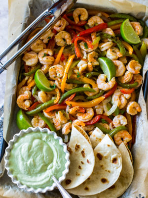 Overhead photo of shrimp and veggies on baking sheet with avocado creama