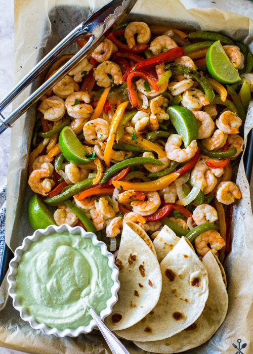 Overhead photo of shrimp and veggies on baking sheet with avocado creama
