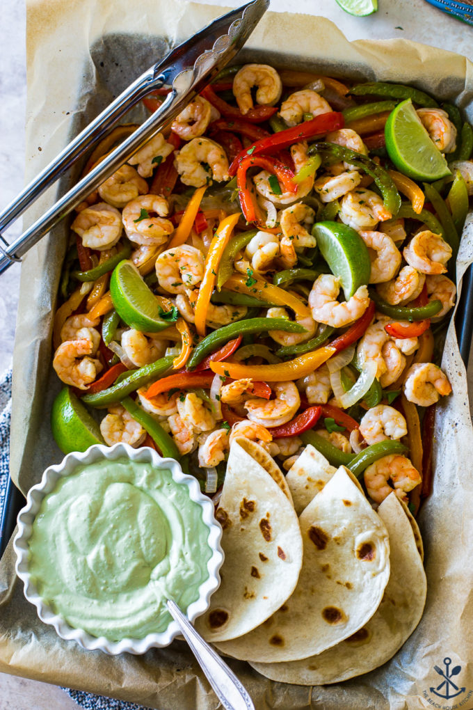 Overhead photo of shrimp and veggies on baking sheet with avocado creama