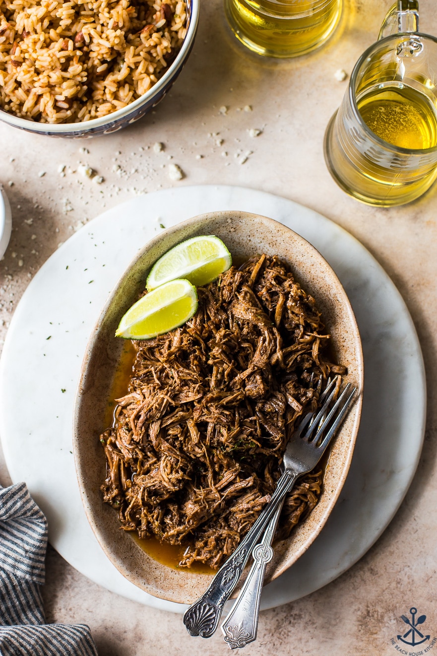 Overhead photo of shredded beef on an oval plate with limes