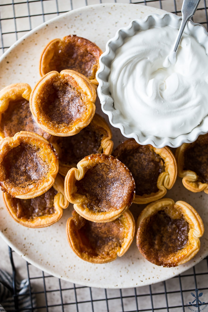 Up close photo if a plate of butter tarts with a bowl of fresh whipped cream