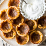 Candian Butter Tarts on a plate with some whipped cream in a bowl