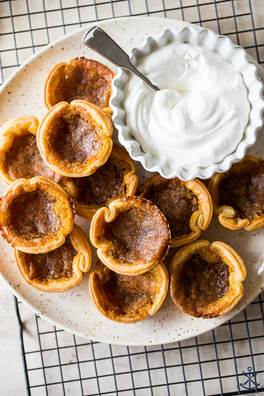 Overhead photo of butter tarts on a plate on a wire rack with a bowl of whipped cream