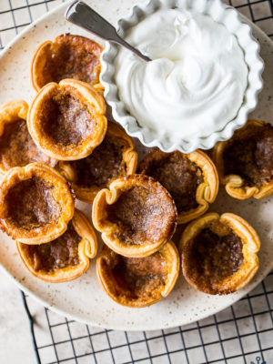 Overhead photo of a plate of Canadian Butter Tarts with a bowl of fresh whipped cream