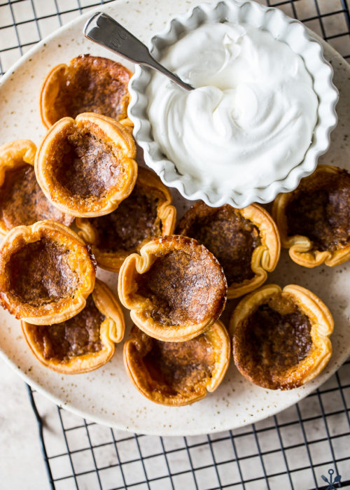 Overhead photo of a plate of Canadian Butter Tarts with a bowl of fresh whipped cream