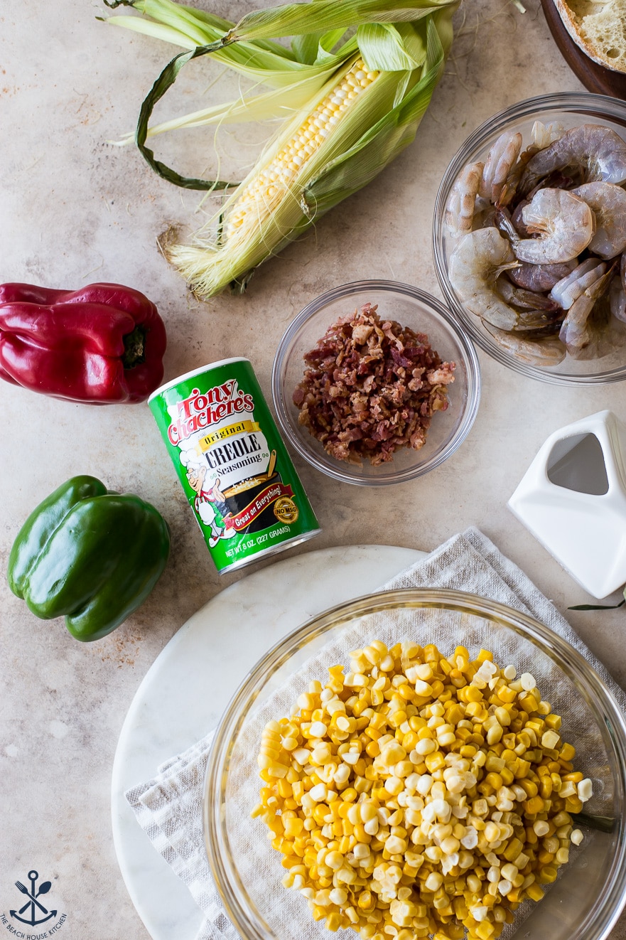 Overhead photo of ingredients for corn dish with shrimp in bowls with a can of creole seasoning
