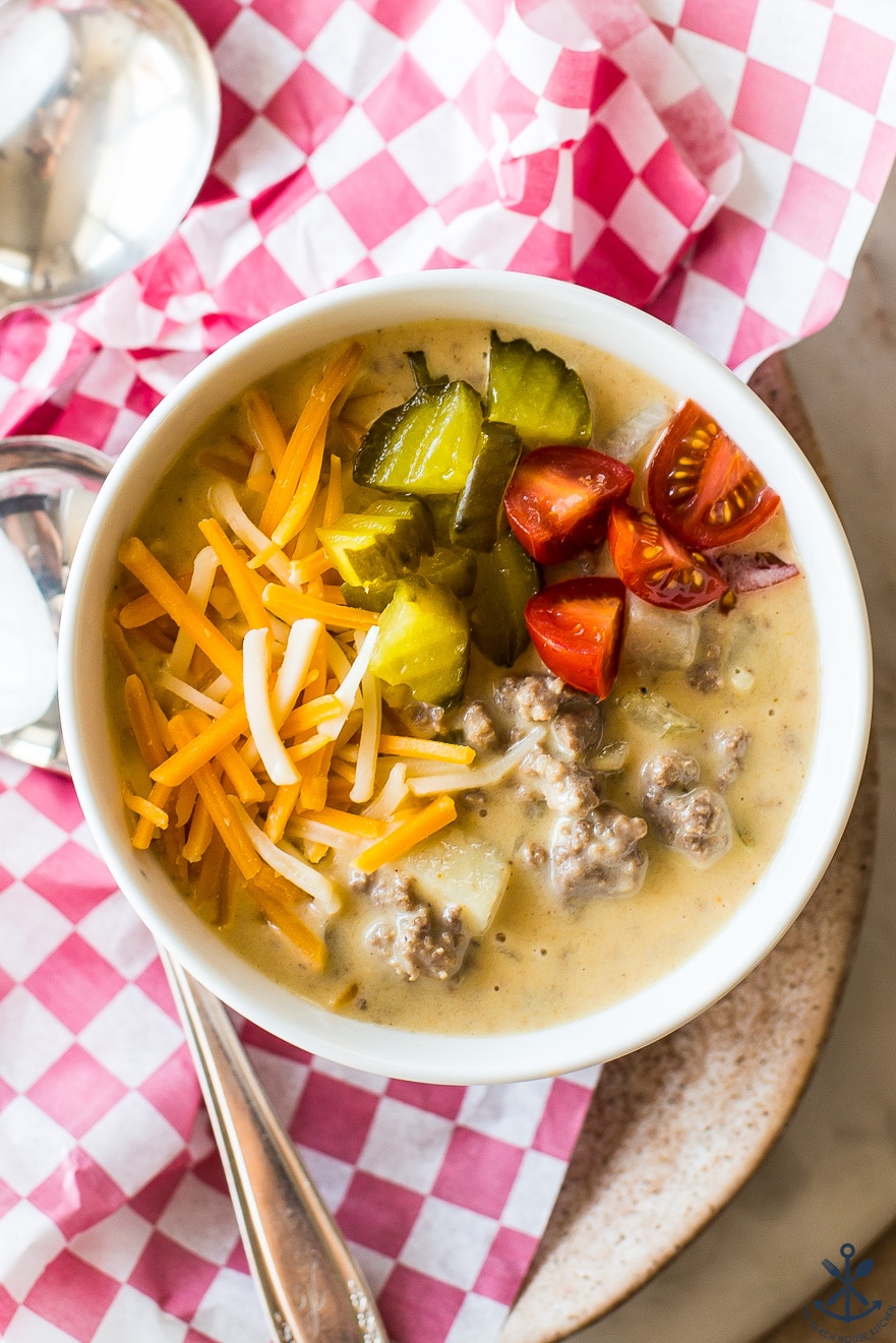 Up close overhead photo of a bowl of cheeseburger soup topped with pickles, shredded cheese and tomatoes