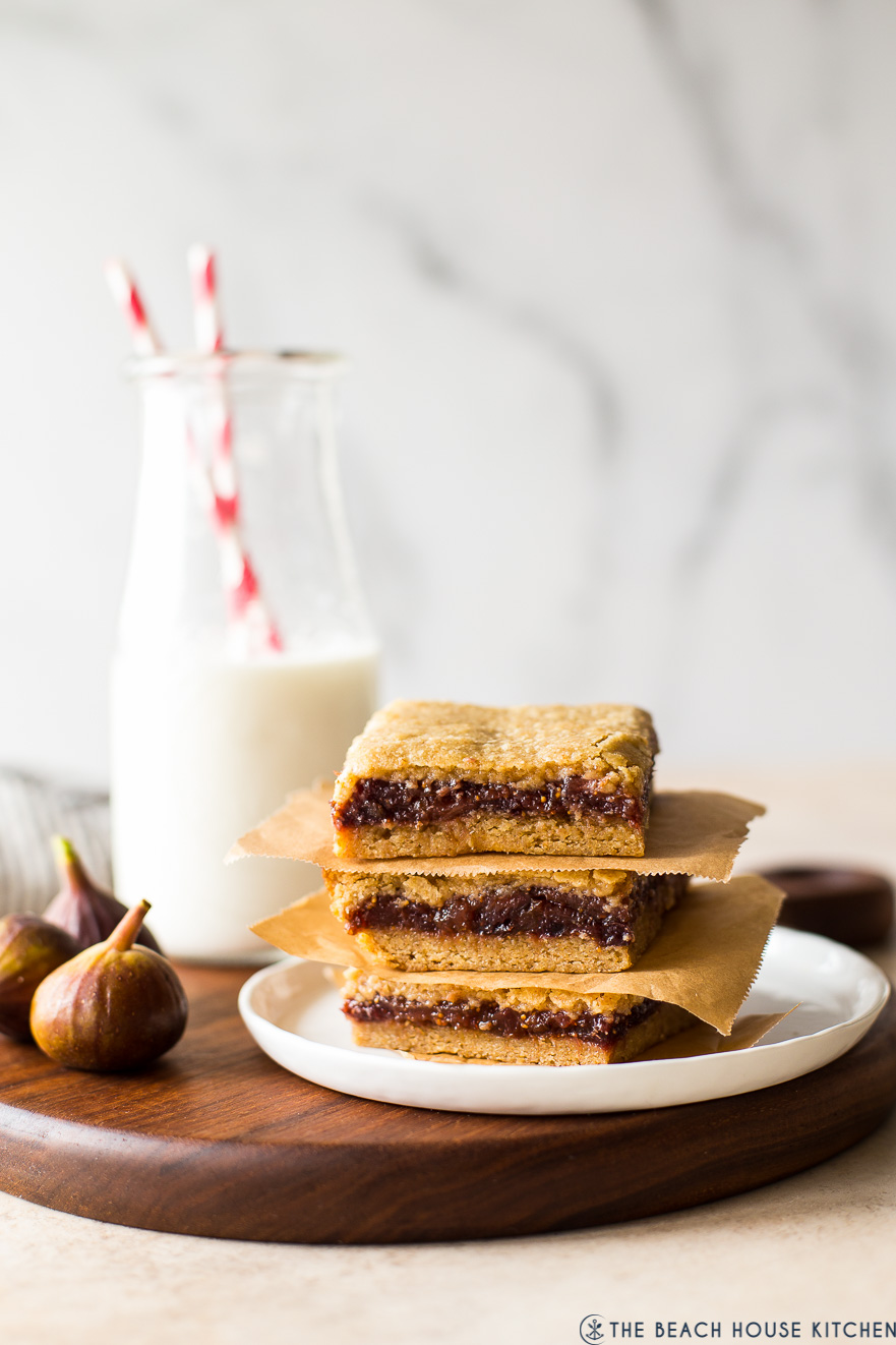 A stack of three fig bars on a white plate with a bottle of milk in the background
