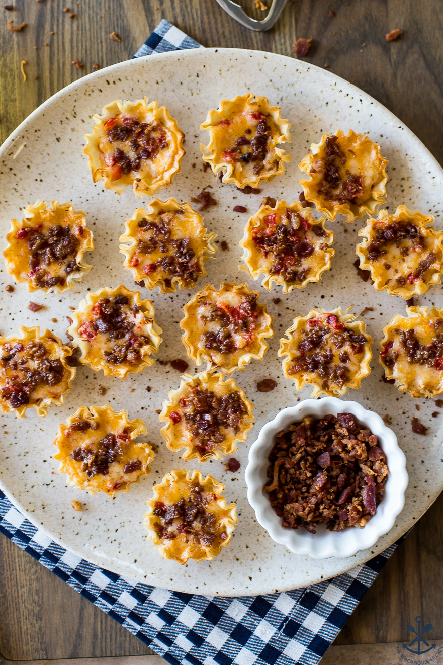 Up close overhead photo of a plate of bacon pimento cheese bites with a small bowl of bacon bits