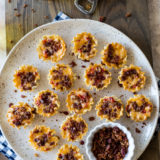 Overhead photo of bacon pimento cheese bites on a plate with a glass of beer and a can opener on a wooden board