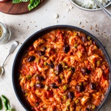Overhead photo of a skillet with with a shrimp mixture with tomato sauce and olives