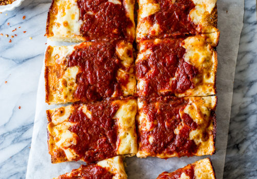 Overhead photo of a pizza cut into squares on a marble board