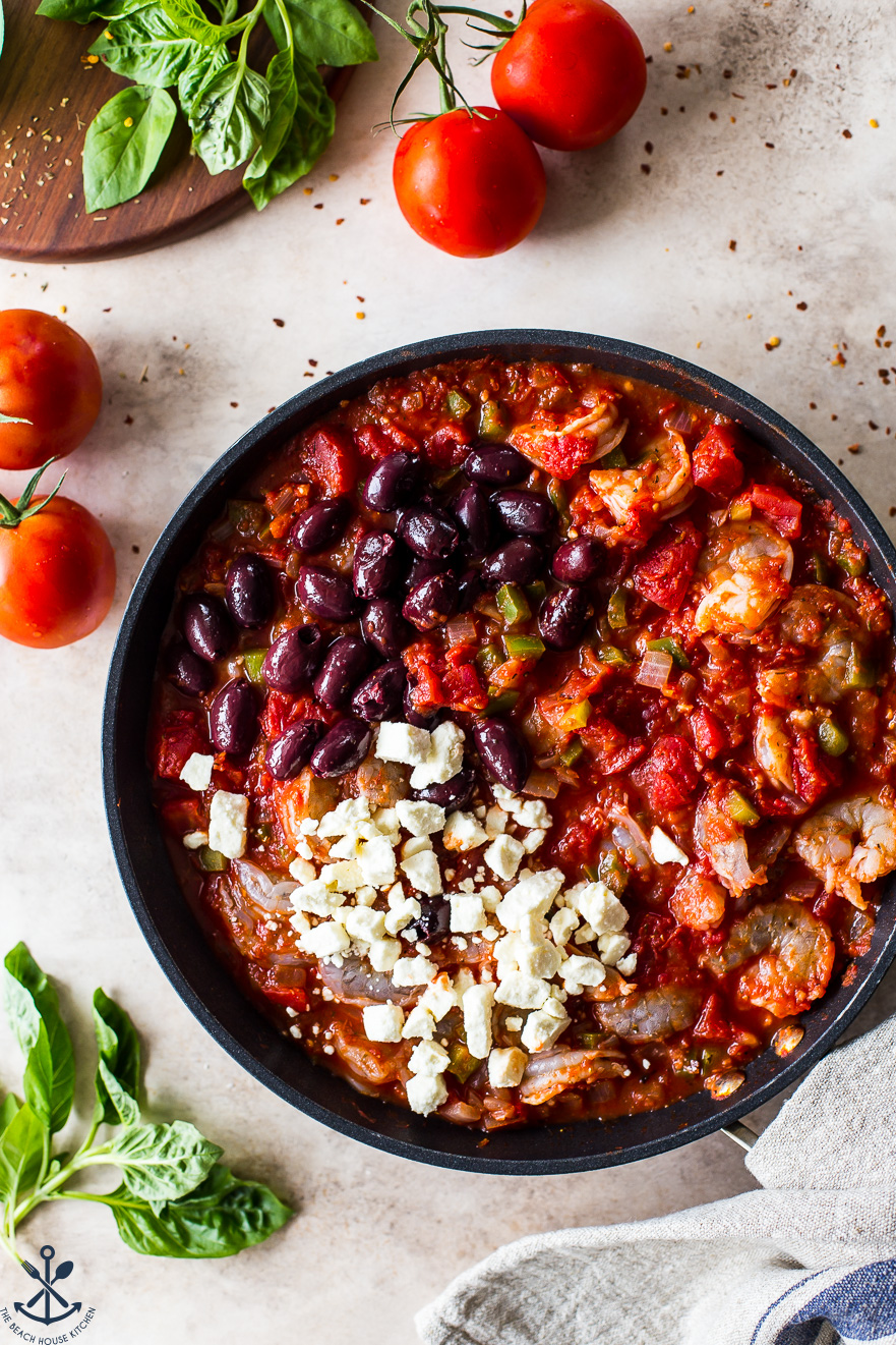 Up close overhead photo of a skillet filled with a shrimp tomato mixture, Kalamata olives and feta crumbles