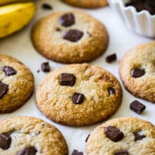 Chocolate chunk cookies with two bananas in the background and a bowl of chocolate chunks