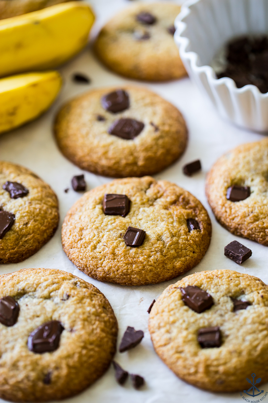 Chocolate chunk cookies with two bananas in the background and a bowl of chocolate chunks