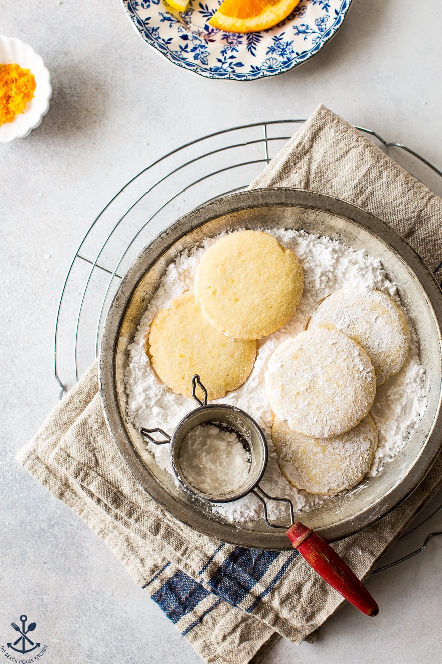 Overhead photo of a pie plate filled with powdered sugar and cookies on a round wire rack.
