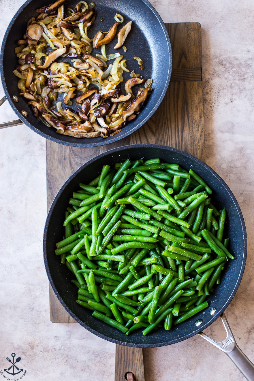 Overhead photo of a skillet filled with fried mushrooms and a skillet filled with green beans