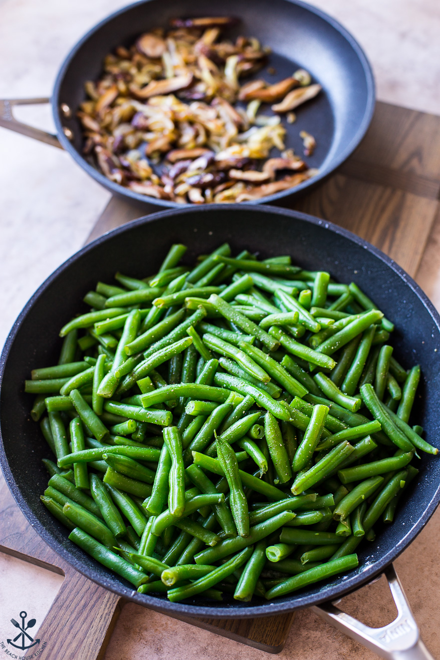 A skillet filled with green beans with a skillet filled with fried mushrooms in the background