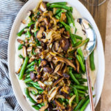 Up close overhead photo of oval plate of green beans topped with mushrooms and onions