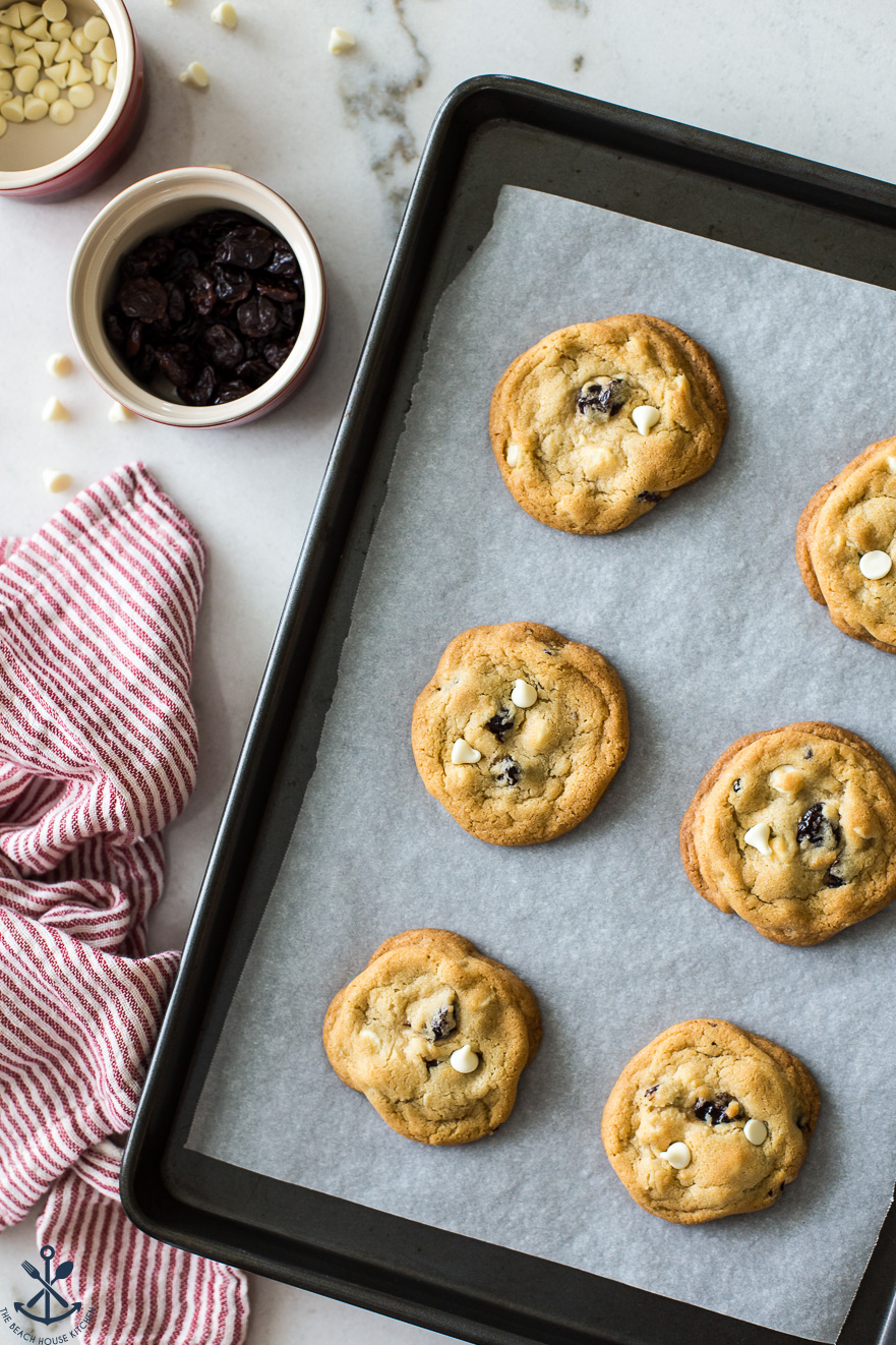 Overhead photo of a parchment-lined tray of cookies with a small bowl of dried cherries off to the side