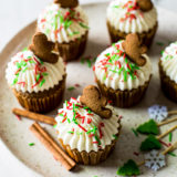 A plate of cream cheese frosted cupcakes with red and green sprinkles topped with a gingerbread man cookie