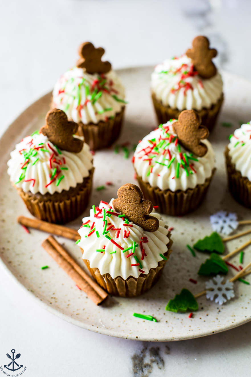 A plate of cupcakes topped with cream cheese frosting and red and green sprinkles topped with a gingerbread man cookie