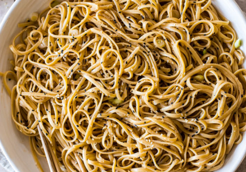 Overhead photo of a round white dish of sesame noodles with chopsticks