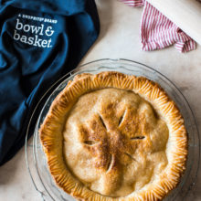 Overhead photo of an apple pie with a blue apron off to the side