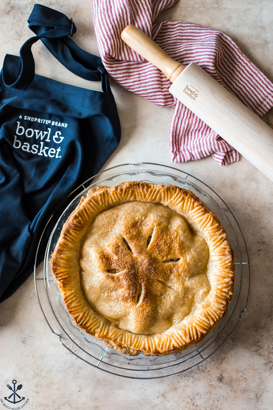 Overhead photo of an apple pie with an apron and rolling pin off to the sides