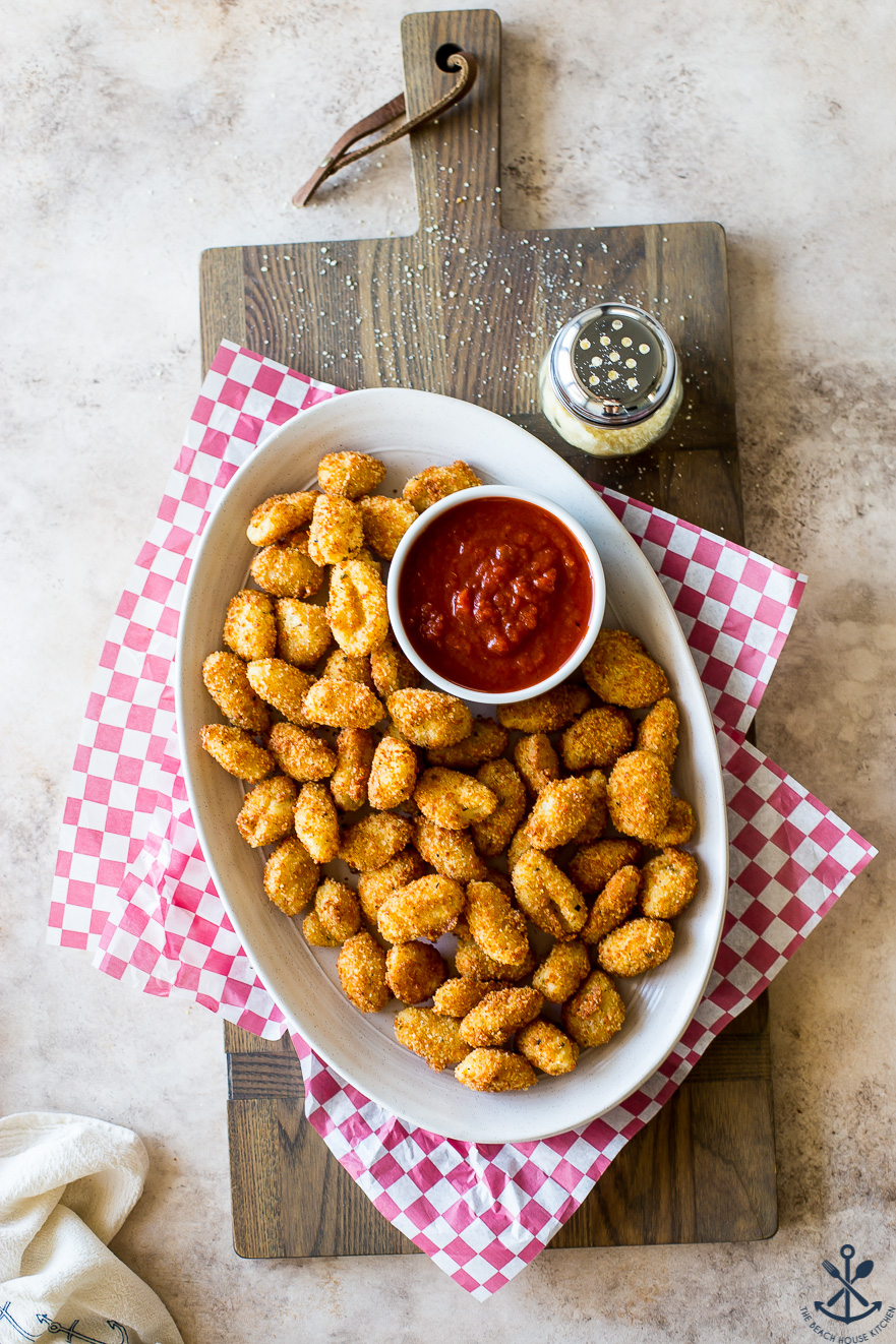 Toasted Gnocchi Bites on a oval plate with a bowl of marinara on red and white checked paper