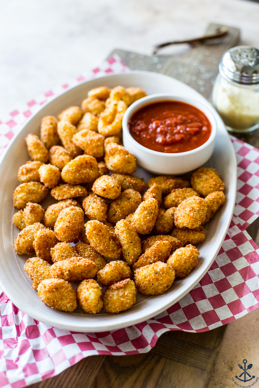 A plate of deep-fried gnocchi bites with a small bowl of marinara sauce