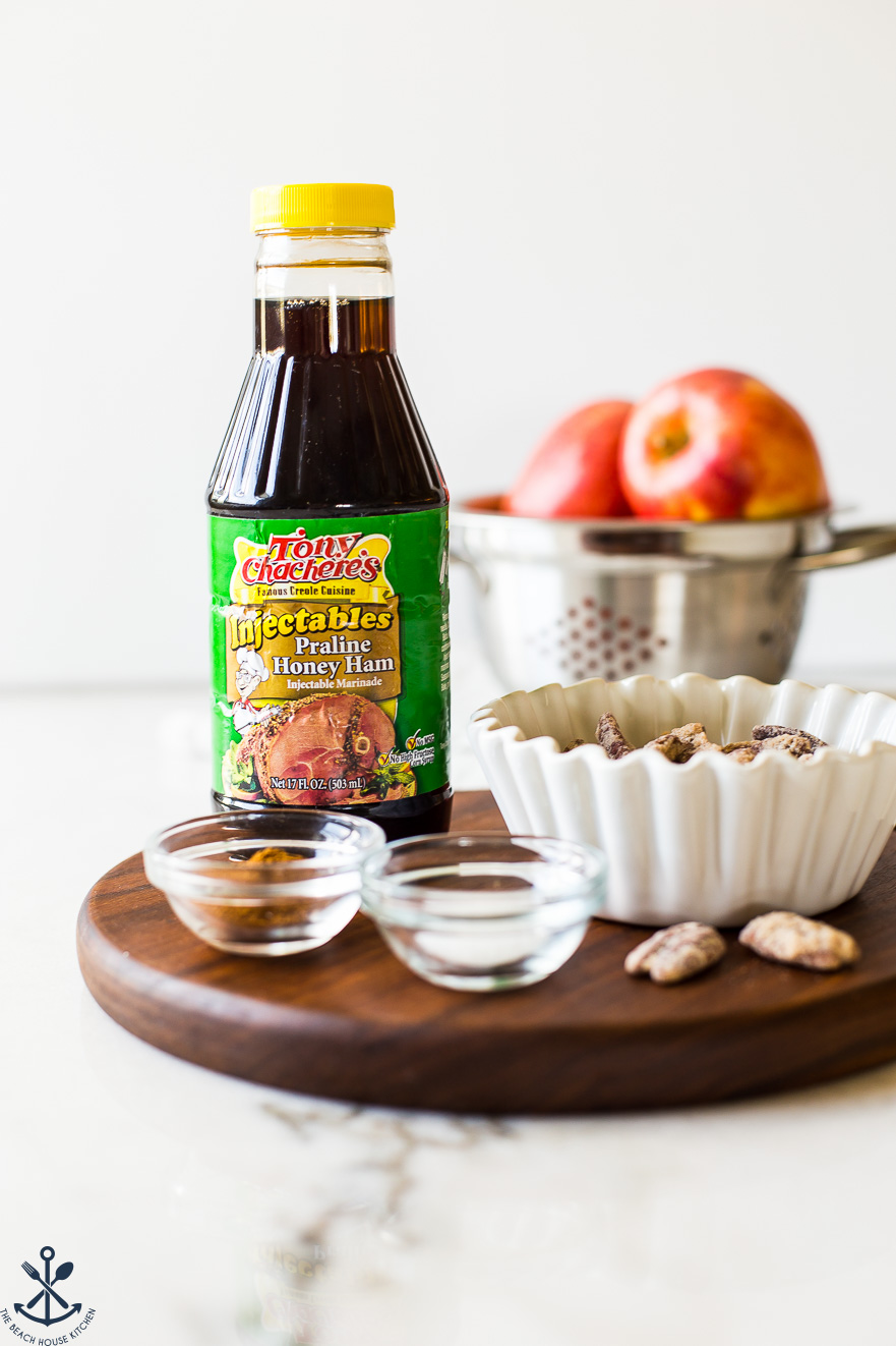 Up close photo of a bottle of praline honey ham marinade on a wooden board with apples in the background