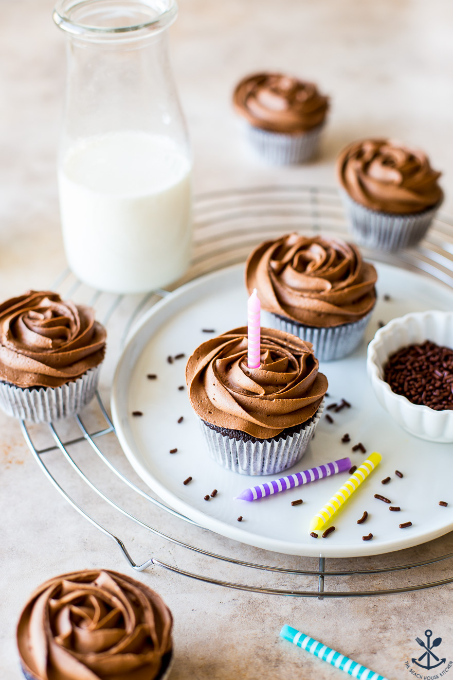 A white plate of chocolate cupcakes with a bottle of milk in the background