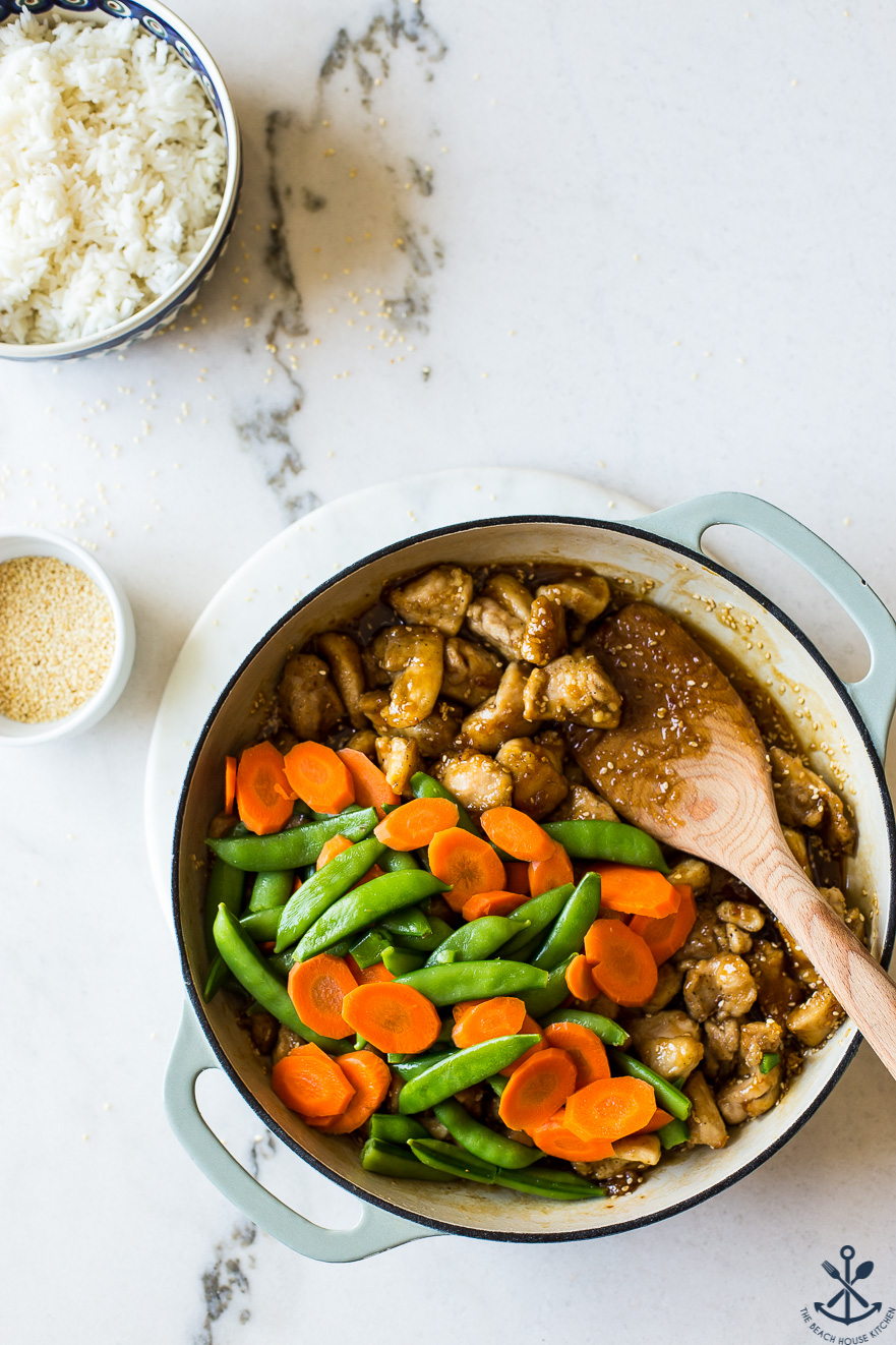 Overhead photo of a skillet filled with sesame chicken, carrots and sugar snap peas