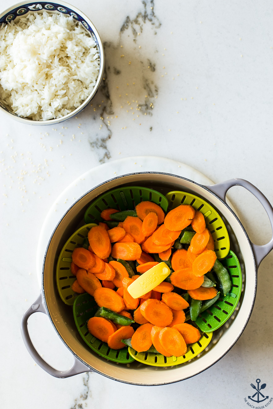 Overhead photo of a pot of steamed carrots and sugar snap peas and a bowl of rice off to the side