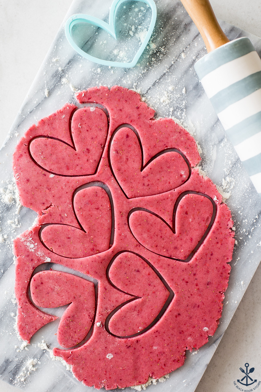 Overhead photo of pink cookie dough with heart cutouts on a marble board